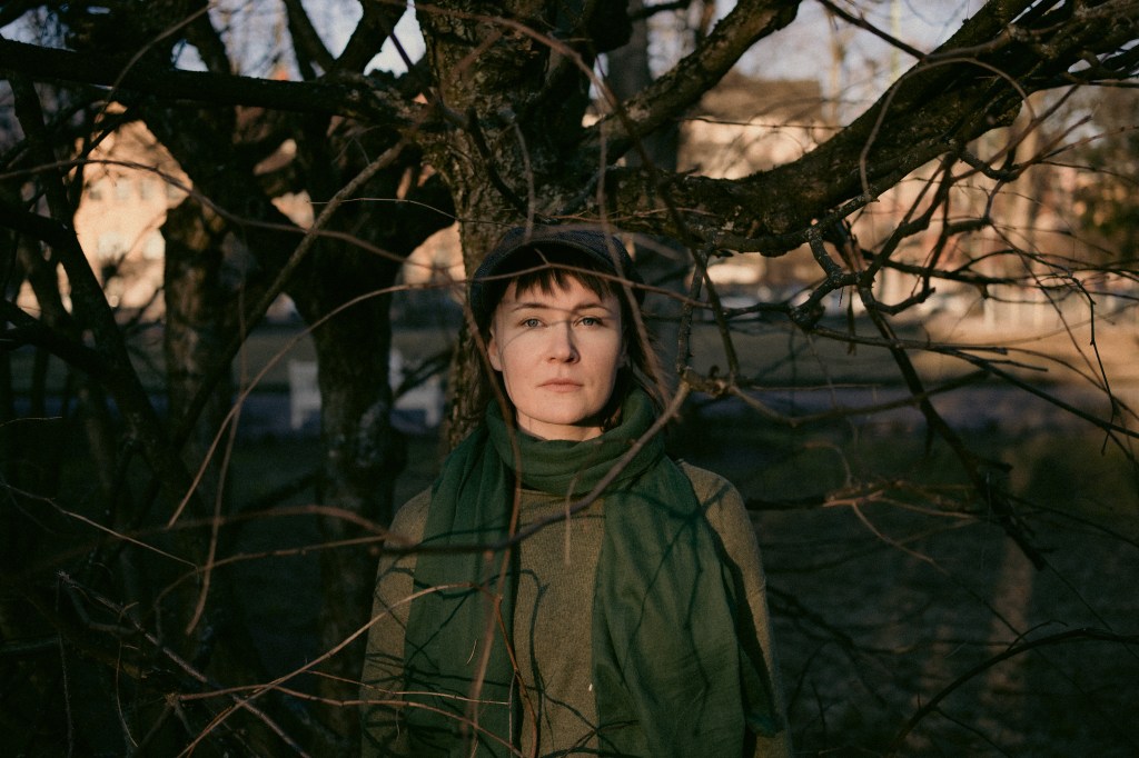 Mirva Ormin looking straight at the camera with barren tree branches shadowing her face.